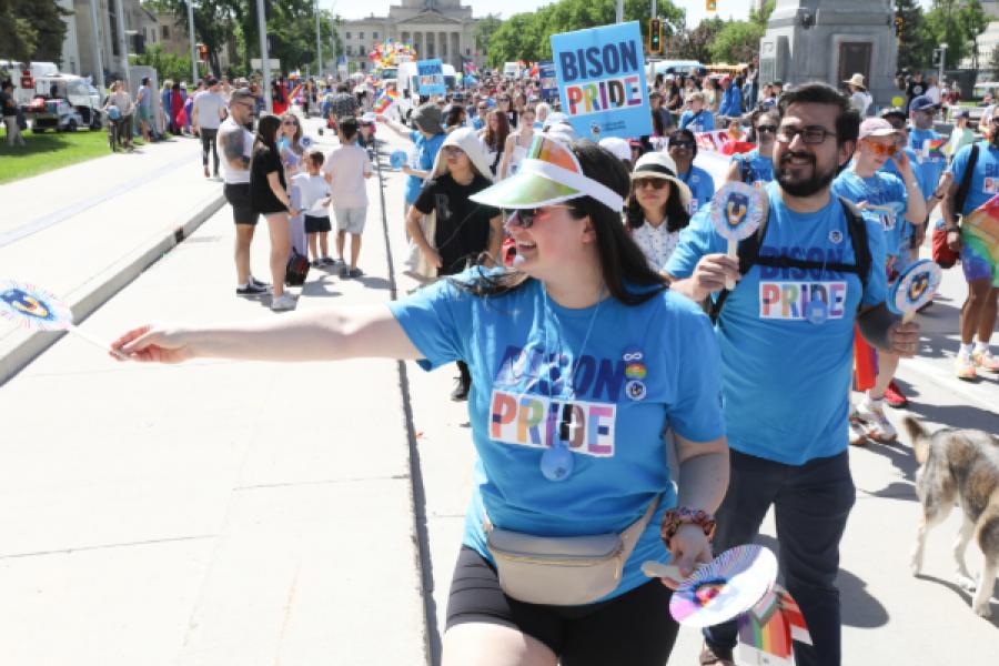 UM participants handing out bison pride sign to crowd at the Winnipeg Pride Parade