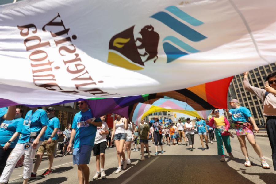 UM flag and Pride flag flying overhead participants in the Winnipeg Pride parade.