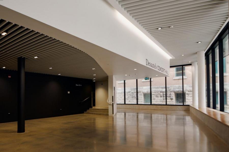 empty lobby featuring large floor to ceiling windows and white walls with entrance to concert hall with dimmer lighting