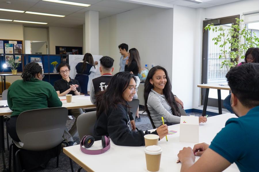 Students sitting in lounge, workshop style at tables.