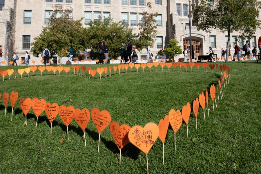 orange paper hearts arranged on the grass in the shape of a heart with trees and a building in the background