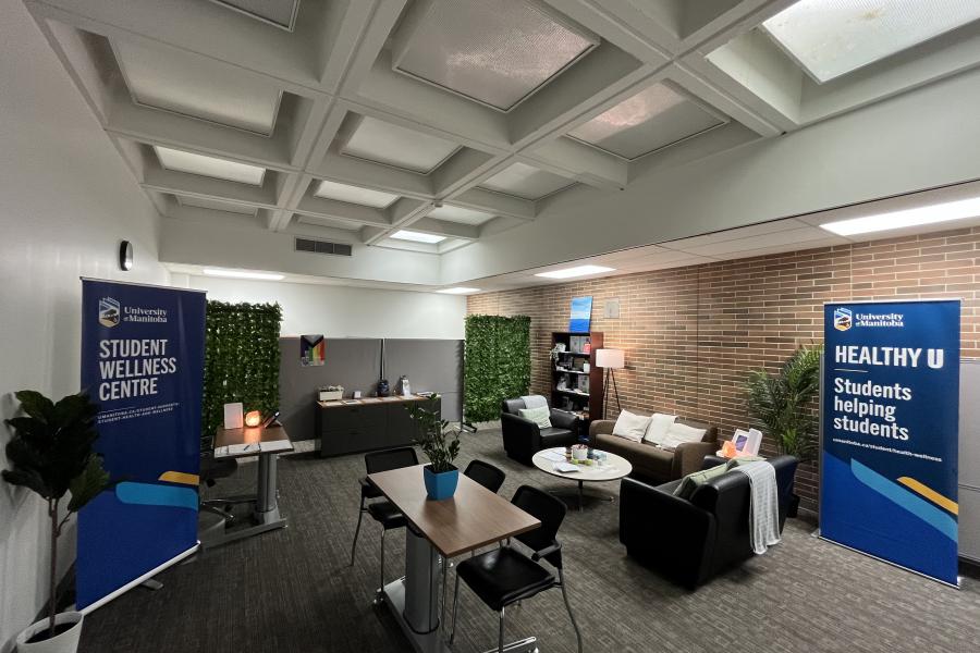 Comfy couches, dim lighting and plants in UM's Student Wellness Centre. One banner says "Student Wellness Centre" and the other says  "Healthy U: Students helping students"