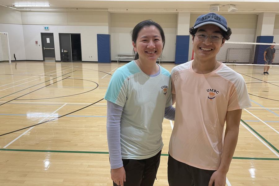 Two students smiling into the camera, wearing UM Badminton Club shirts 