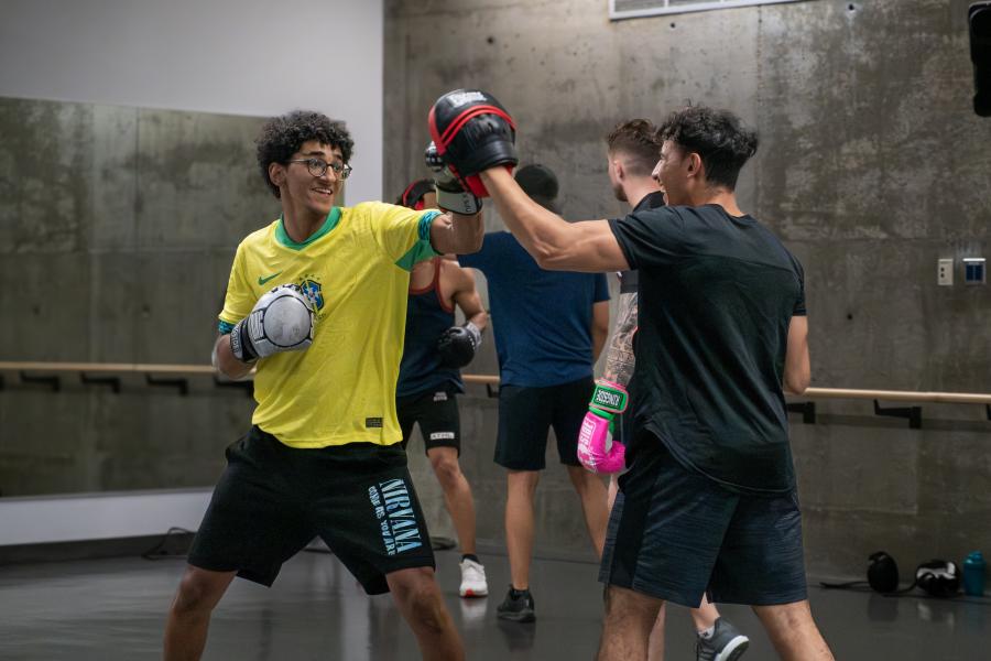 A man in a yellow shirt practices boxing punches with a partner