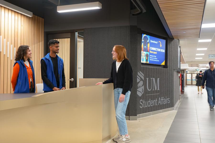 a student standing on the right side of a desk, talking to two student staff who are dressed in blue and answering questions