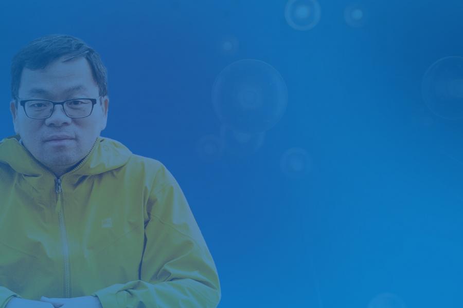 photo of man on left of screen, wearing a yellow rain jacket and wearing glasses. Image set agains blue background 