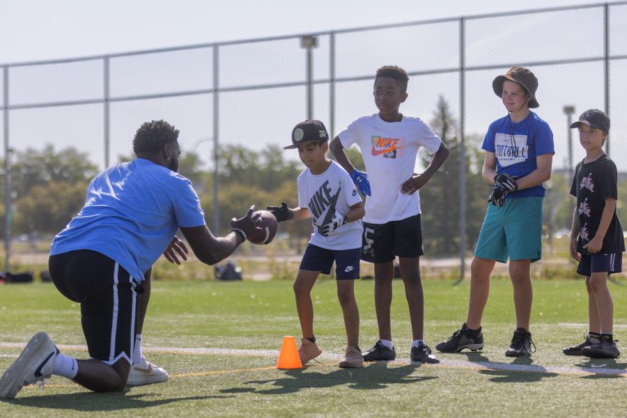 A mini u leader passing off a football to a camper