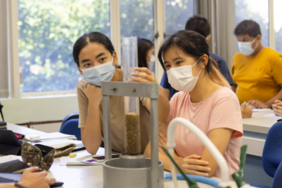 young students with face mask do hydraulic test of samples, note, analyze data using notepad, computer, tablet, phone, calculator in classroom or science laboratory in university