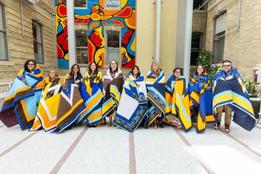 Ten individuals stand on a stage wrapped in star blankets.