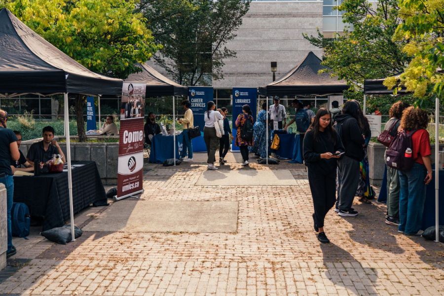Students visiting outdoor information booths with tents, banners, and tables set up for campus services and clubs.