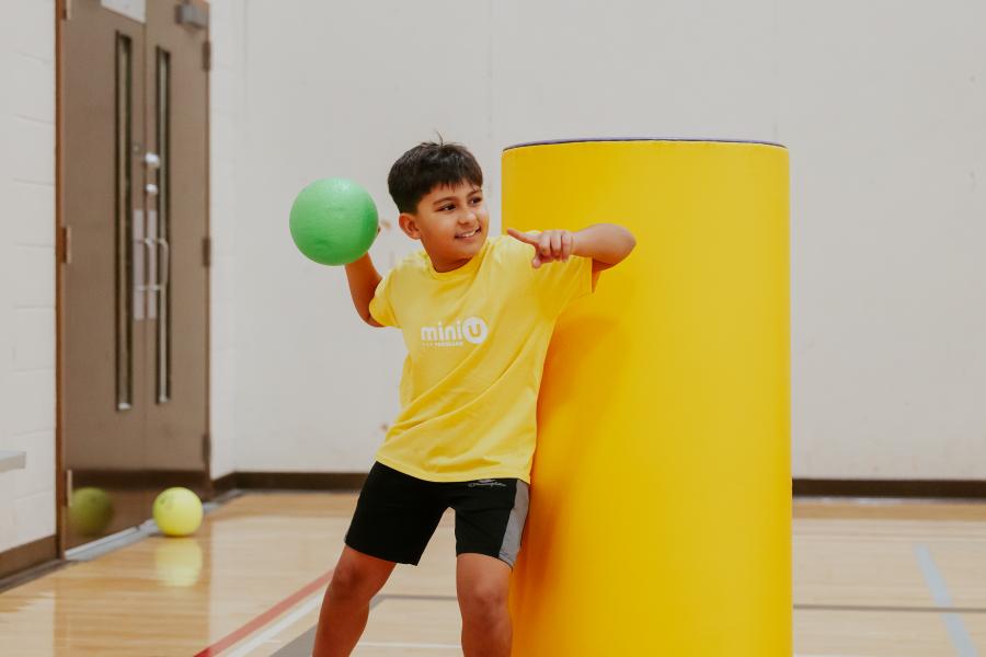 A mini u camper winding up a dodgeball throw in a gym