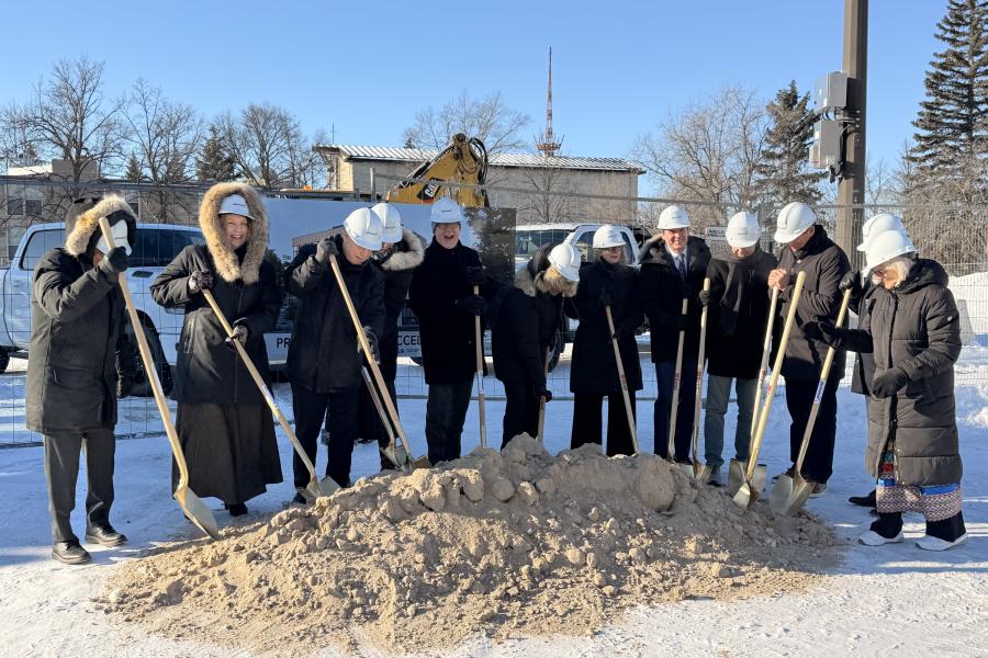 A group of people holding shovels for a ceremonial groundbreaking photo outside on a cold, sunny winter winter day.