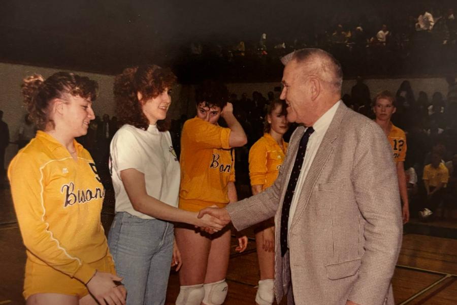 Four Bisons volleyball athletes lined up and shaking hands with the president of the university.