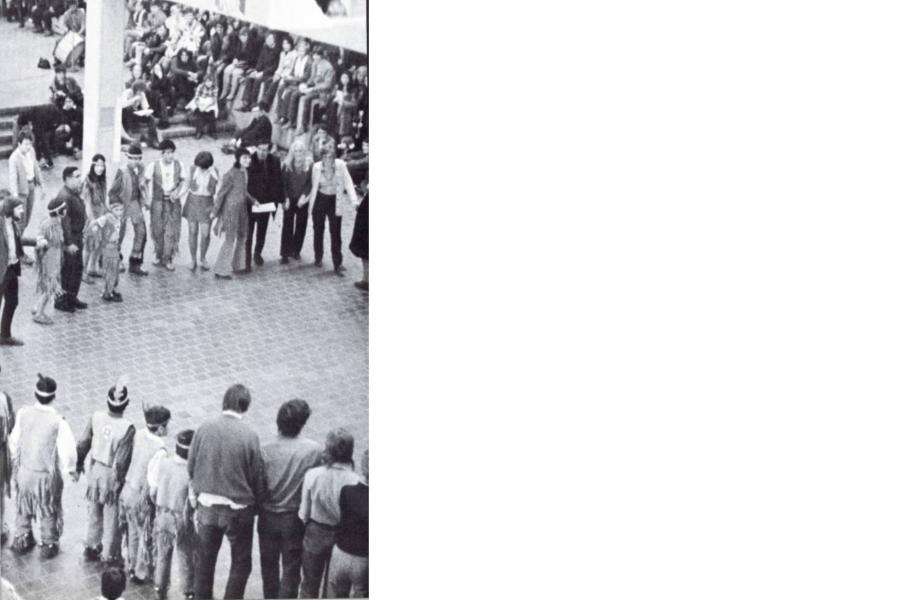 A large crowd holding hands and making a circle, wearing cultural regalia at the first University of Manitoba Pow Wow in 1972.