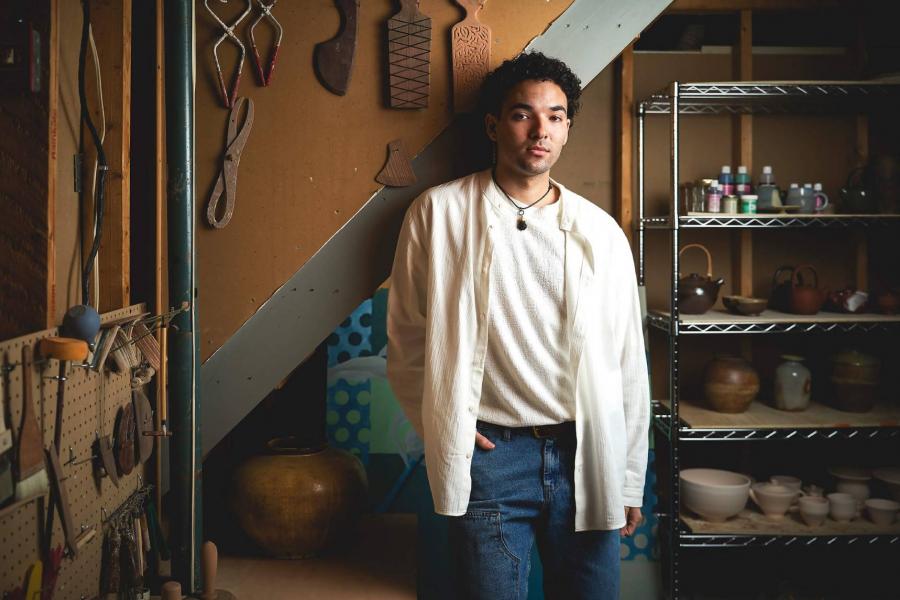 Joel Nichols standing in a workshop next to tools and pottery on shelves.