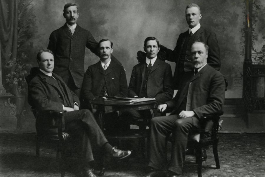 Six men dressed in suits posing for a photo, they are University of Manitoba's first faculty members.