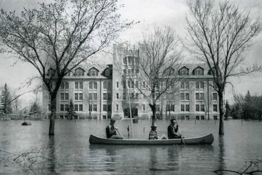 Three people paddling a canoe across University of Manitoba's Fort Garry campus during the 1950 flood.