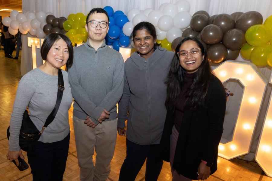 four people posing in front of a balloons and marquee light up letters.