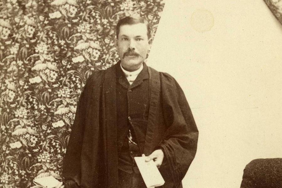 William Reginald Gunn posing in his grad gown and holding his degree in 1880.