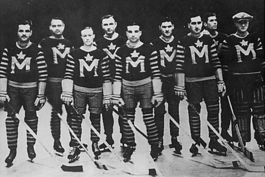 Nine players in full hockey gear standing on the ice. They are the University of Manitoba Grads hockey team in 1931.