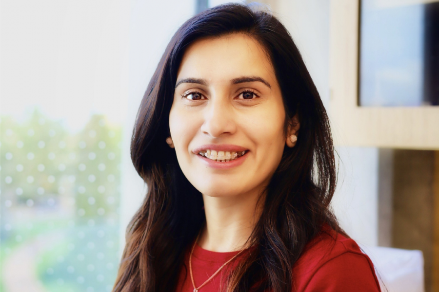 Smiling woman in a red top standing near a bright window.