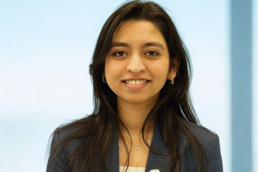 Smiling woman in a navy blazer standing against a softly lit background.