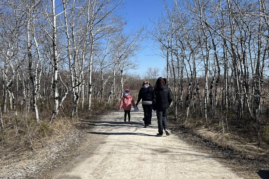 A trio of people on a dirt path viewing native bird species at Fort Whyte Alive.