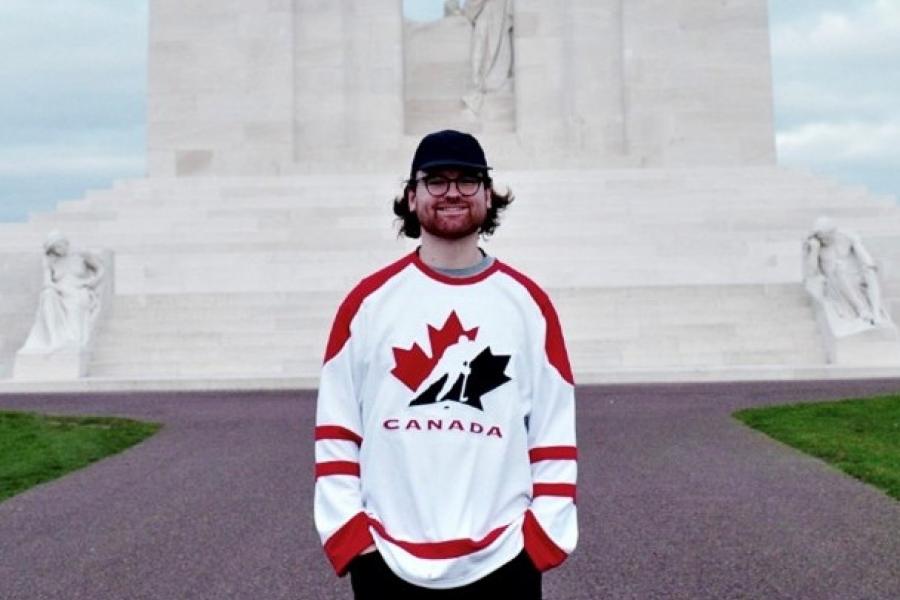 Jayden, standing in front of a tall structure and smiling on camera.