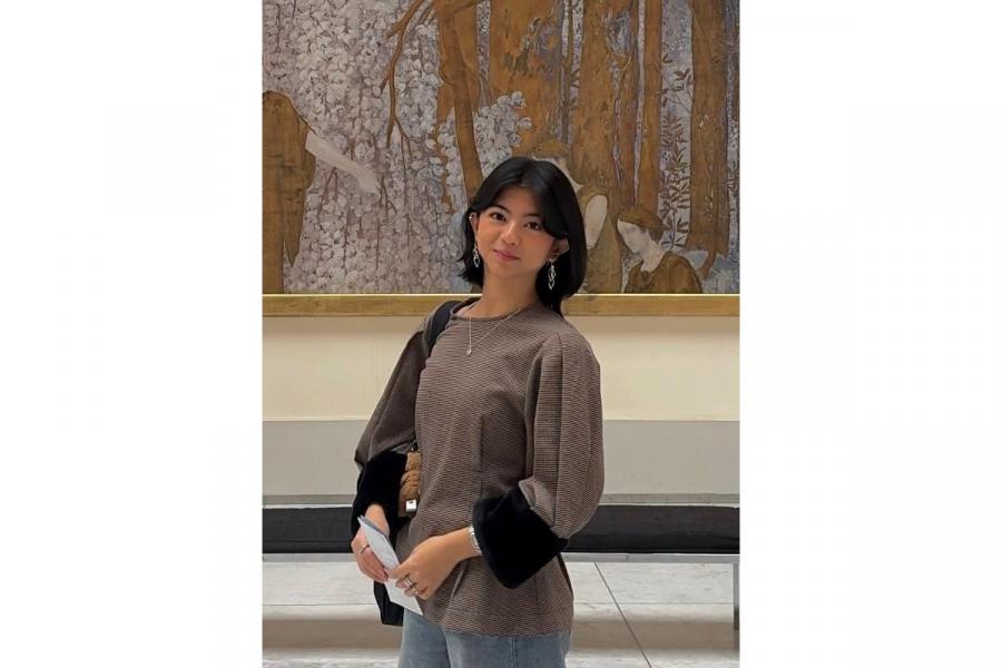 Justine, standing in front of a large painting smiling slightly at the camera.