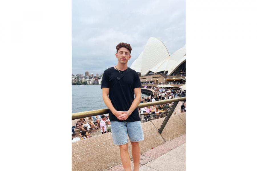 Kyle, leans against a railing while overlooking the harbour with the Sydney Opera House in the background.