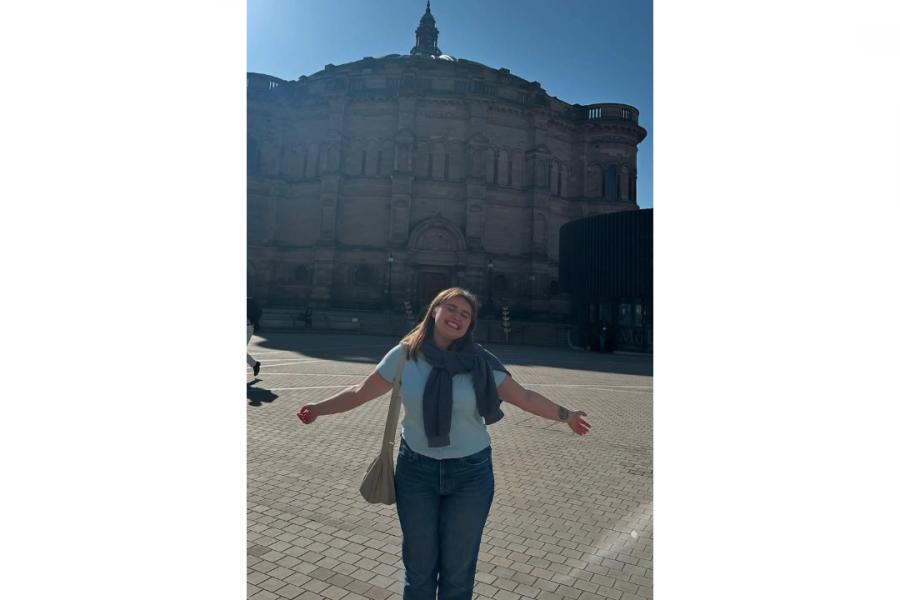 Morgan posing in front of a structure on a sunny day with both arms raised.