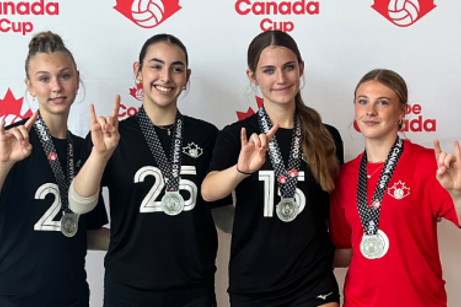 Four players from Junior Bisons girls volleyball teams make a "horns up" symbol with their hands infront of a Volleyball Canada background.
