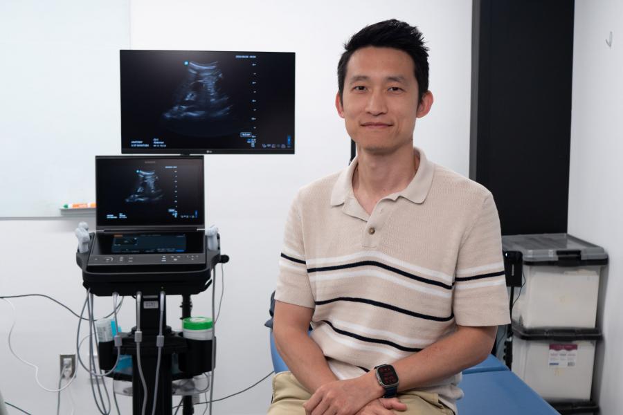 Terry Li sits next to an ultrasound probe and monitor.