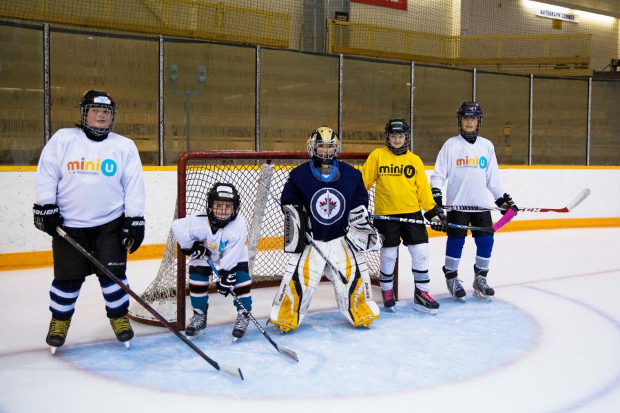 A group of five hockey players stand at the net.
