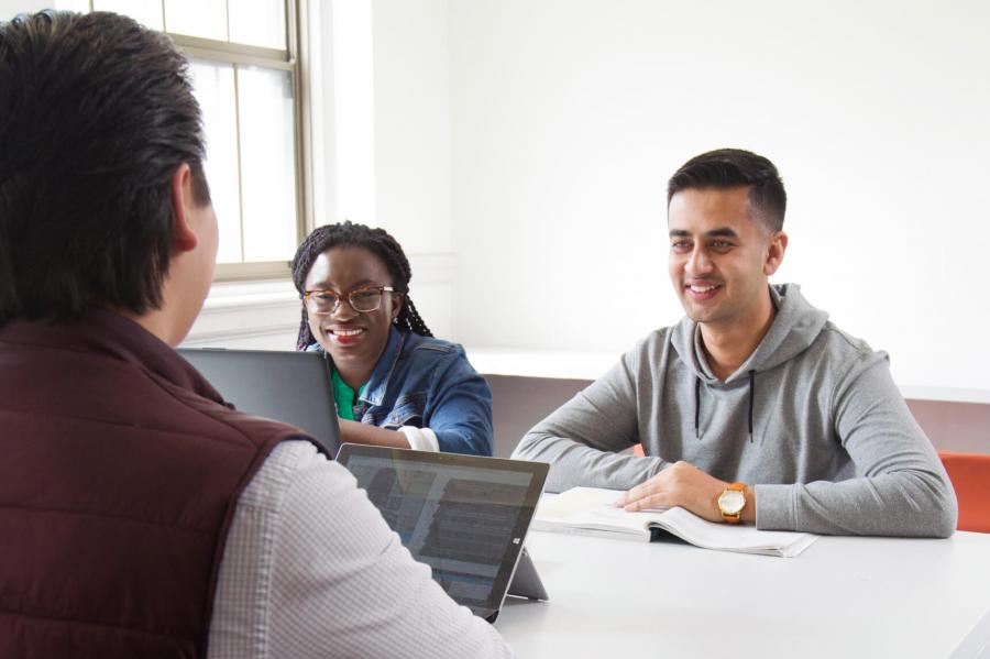 Three smiling students sitting at a desk studying together.