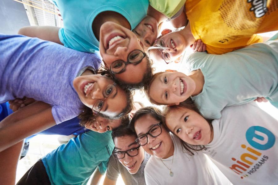 A large group of children huddle together in a circle with their heads together to pose for a photograph.