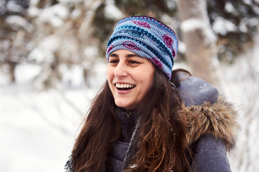 An international student smiles and laughs happily while standing outside on a snowy winter day. 