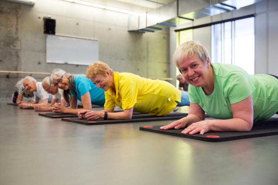 Senior Active living centre members perform low planks while participating in a group Aging actively fitness class.