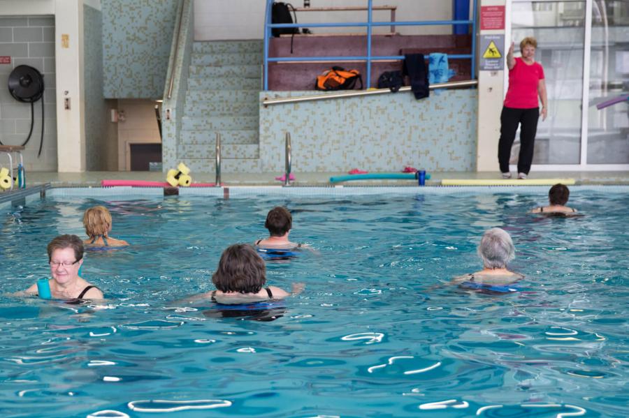 A group of adult swimmers in the pool following their group fitness instructors instructions. 