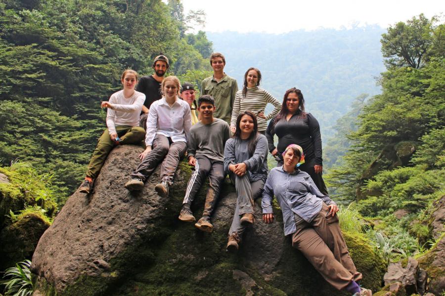 A group of students sit together on a large rock in the Amazon rainforest.