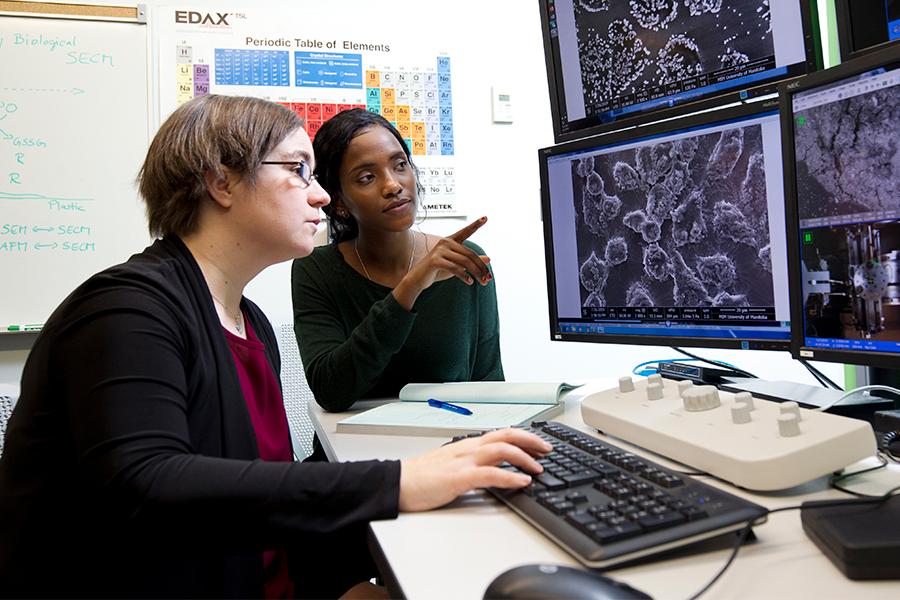 Two UM staff reviewing a microscopic image on four monitors.