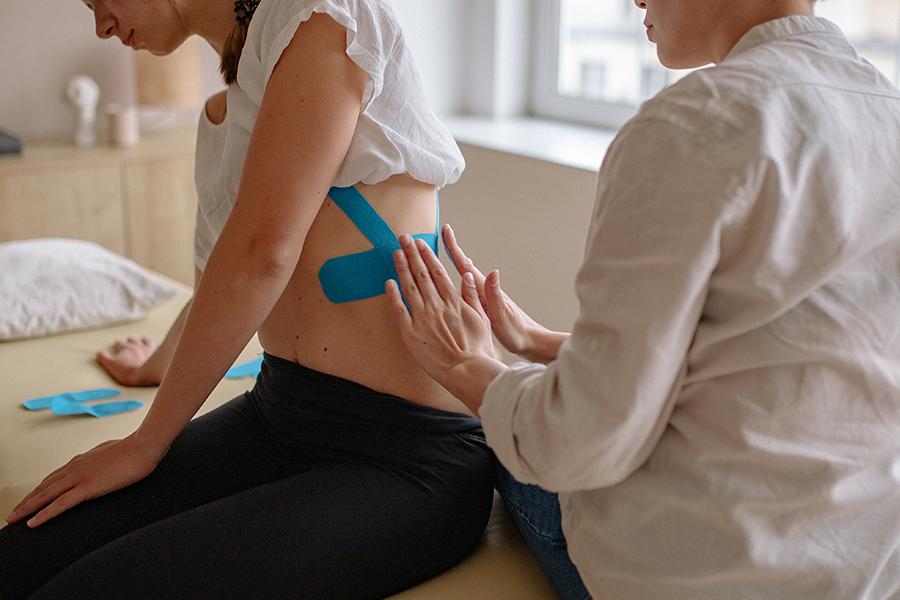 A health care provider placing a therapeutic tape on a patient's back.