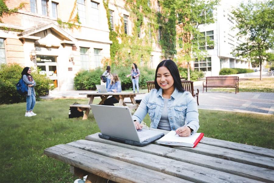 A student sits with her laptop at a picnic table near the Engineering Building.