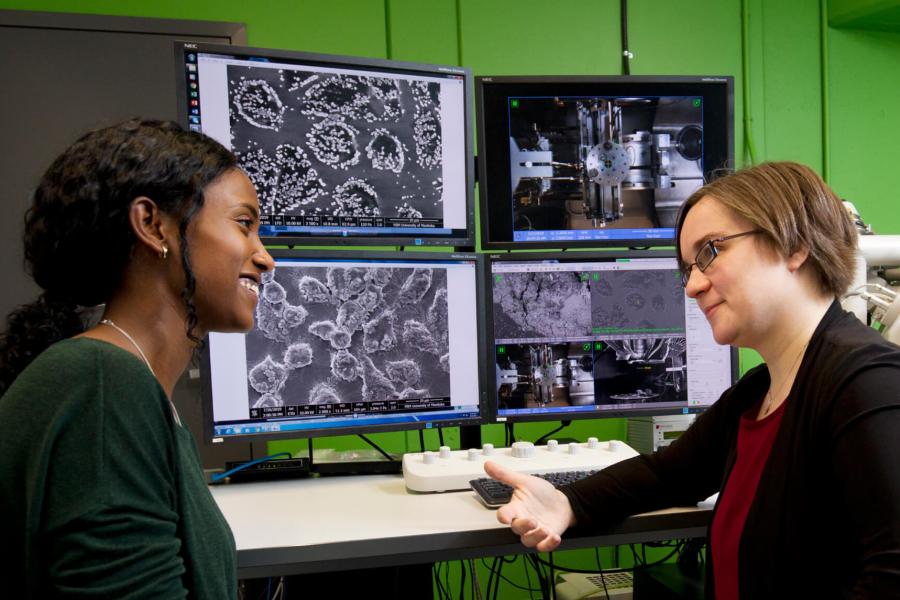 Two researchers sitting together in front of four large monitors in a lab talking. 