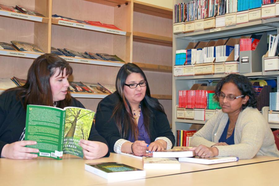 Three students sitting at a table together in a library studying.