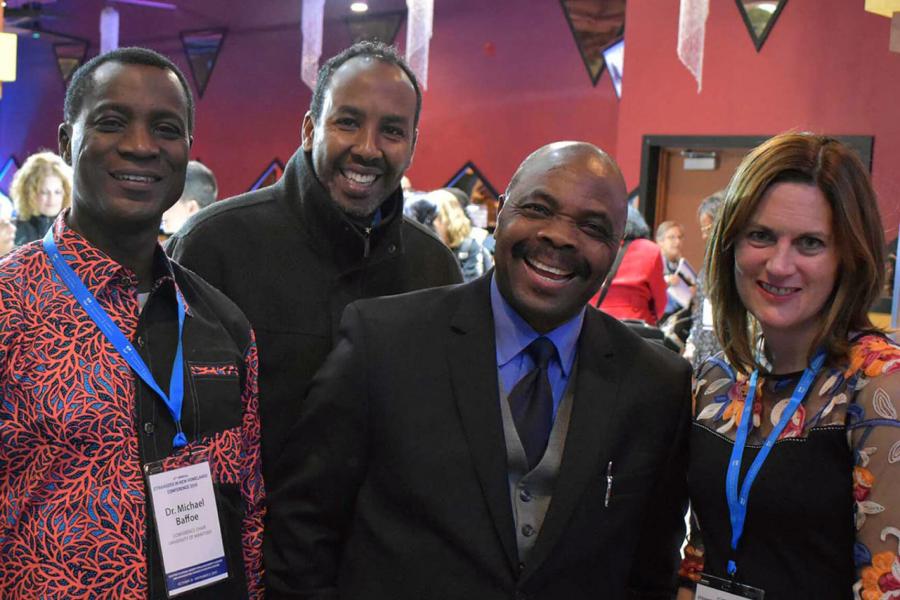 A group of 4 people stand together at a Strangers in New Homelands Conference.