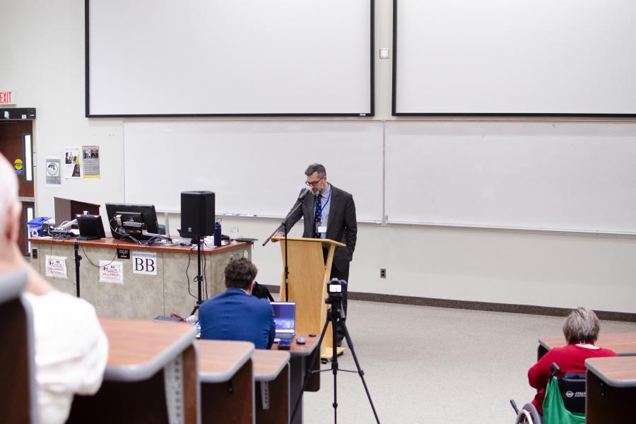 Dr. Justin Stratis standing in front of a podium, delivering his lecture.