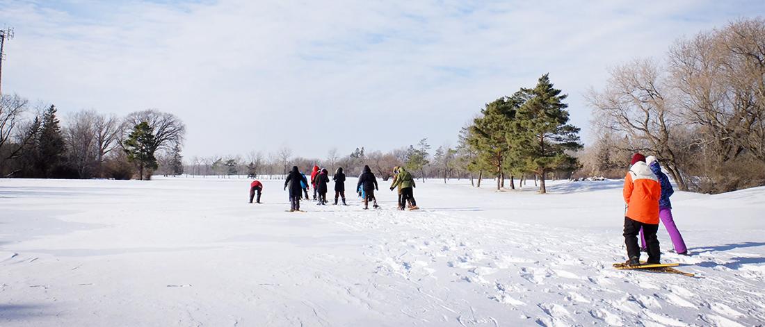 A group of people participate in the Jack Frost Challenge by snowshoeing in an open area at the University of Manitoba Fort Garry campus.