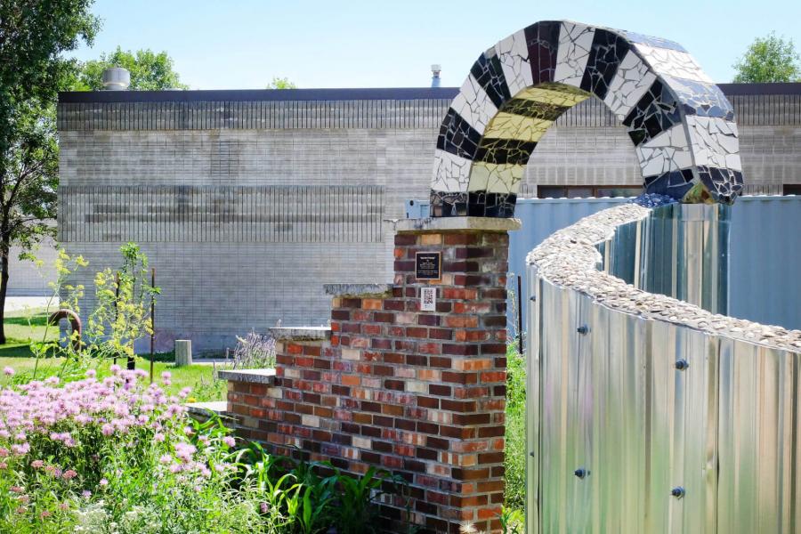 The permaculture garden features flowers and a brick archway. 