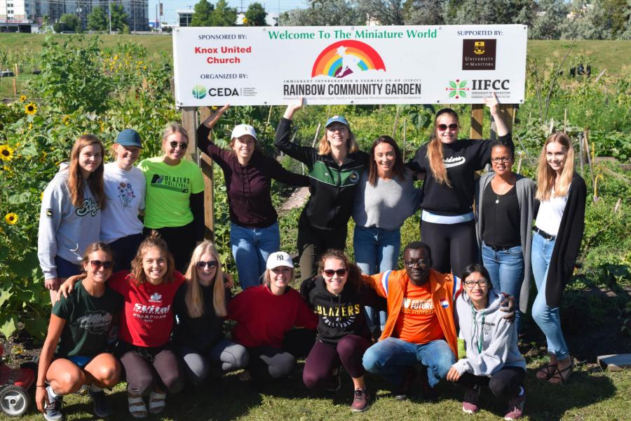 A large group of people huddle together for a photo holding a sign got the Rainbow Garden.